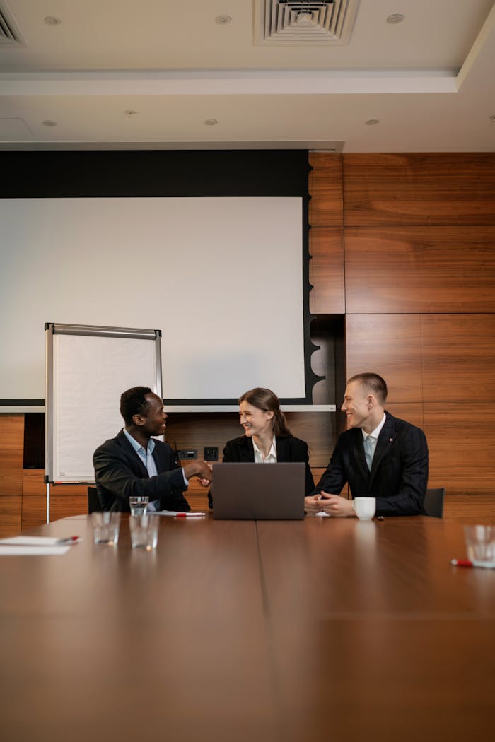 gallery-5 Three professionals engaging in a handshake during a business meeting in a modern office setting.